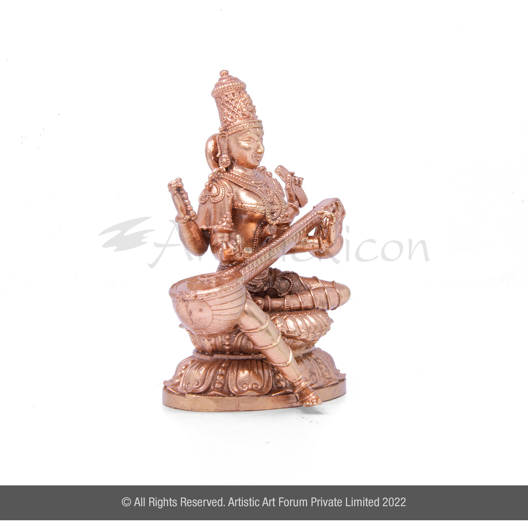 A bronze metal idol of Goddess Saraswati, depicted with four hands, sitting on a structure, with a veena musical instrument. The idol has a glossy finish.